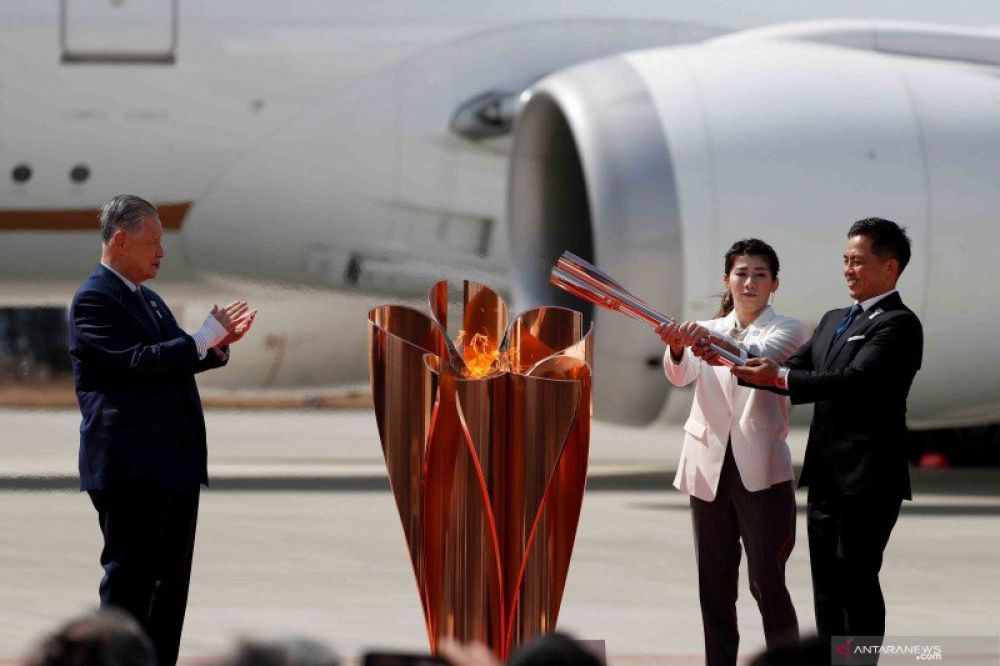 Presiden Olimpiade Tokyo 2020 Yoshiro Mori (kiri) menyaksikan dua atlet peraih tiga kali medali emas olimpiade Tadahiro Nomura (kanan) dan Saori Yoshida menyalakan obor Olimpiade Tokyo 2020 saat tiba dari Yunani di Pangkalan Udara Matsushima di Higashi-Ma