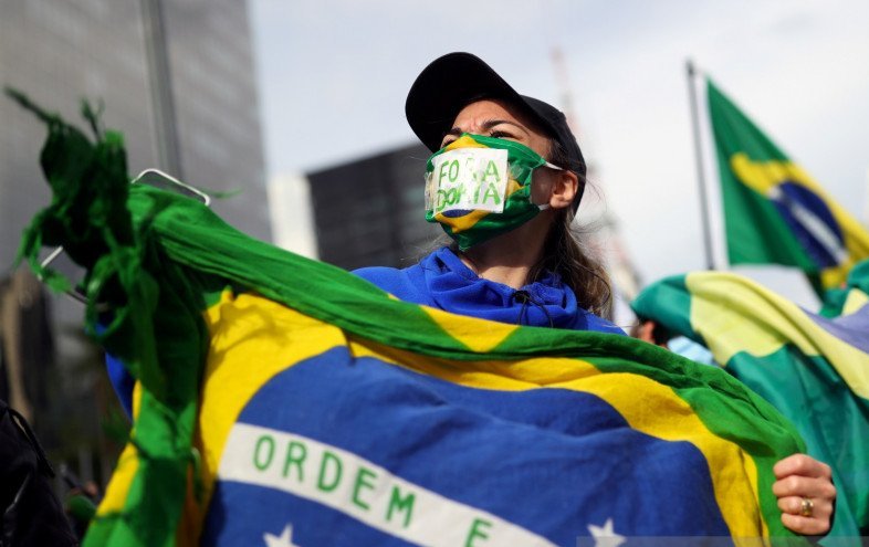Pendukung Presiden Brasil Jair Bolsonaro memakai masker pelindung sambil membawa tulisan pada aksi protes menentang aturan karantina ditengah wabah penyakit virus corona (COVID-19), di Sao Paulo, Brasil, Minggu (24/5/2020). Tulisan pada papan "Doria Out".