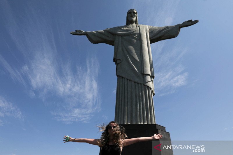 Seorang wisatawan berpose dengan lengan terbentang untuk foto saat pembukaan kembali patung "Christ the Redeemer" setelah ditutup selama beberapa bulan akibat penyebaran penyakit virus korona (COVID-19) di Rio de Janeiro, Brazil, Sabtu (15/8/2020). REUTER