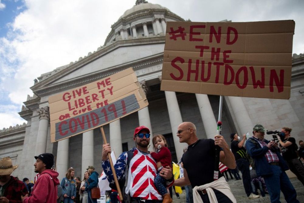 TAK MAU TINGGAL DI RUMAH: Dua pria memegangi karton yang ditulisi saat mereka turun ke jalan bersama ratusan demonstran lainnya di gedung kapitol di Olympia, Washington, Minggu (19/4/2020). Mereka memprotes perintah "di rumah saja", yang diberlakukan peme